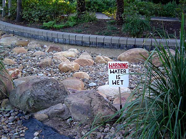 sign in front of dry creekbed reading Water Is Wet